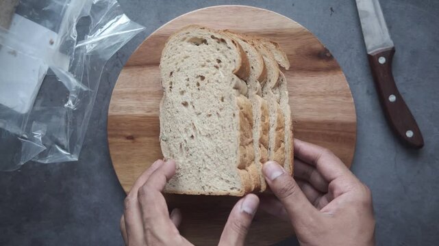 A motion of hand arranging fresh whole wheat bread slices on a round wooden cutting board with a knife on the side, creating a dynamic visual clip