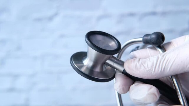 Gloved hand holding stethoscope against white brick background showing medical professional at work in cinematic motion footage clip