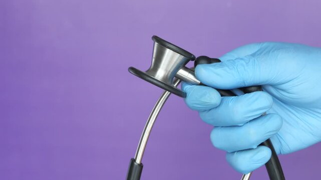 Close-up shot of a hand in a blue medical glove holding a stethoscope against a vibrant purple background