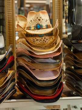 Woven straw and leather cowboy hats with bead bands stand in tall stacks on a glass shelf. Selling hats as a Western fashion country souvenir.
