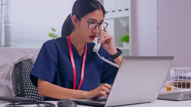 Medical Professional Healthcare Worker Wearing Glasses Using Laptop Reviewing Patient Information Clinical Office Administrative Work, Asian Female Medical Worker Typing Laptop and Telephone During