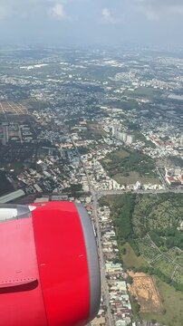 Aerial view of urban landscape of Ho Chi Minh City, Vietnam, with residential buildings and greenery, airplane wing and engine visible in the foreground. Slow motion vertical footage, 4K, copyspace