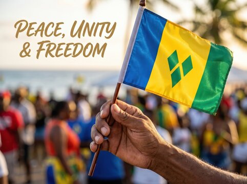 Close up of a hand holding a saint vincent and the grenadines flag with text peace unity and freedom against a blurred outdoor crowd background