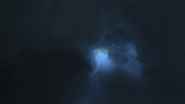 Dark storm clouds conceal glowing blue light in night sky.