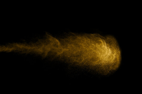 Golden powder particles form a flowing abstract cloud against a deep black background, creating a luxurious dust effect with motion and texture for beauty, celebration, energy, and creative design.