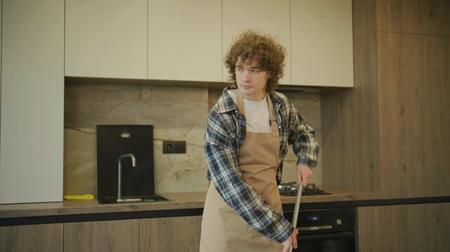 Person mops the floor in a modern kitchen while wearing an apron and a plaid shirt during the day