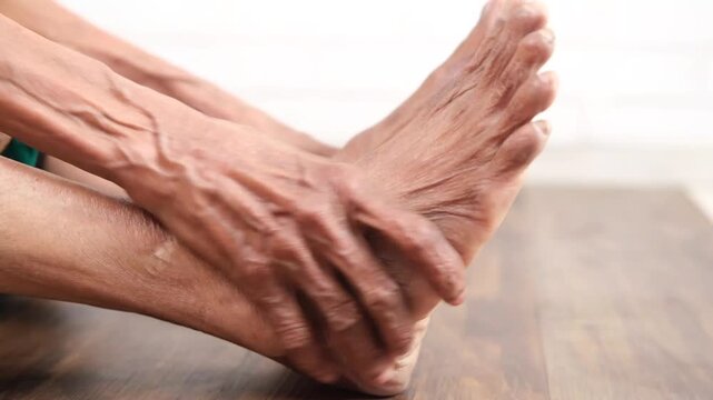 Elderly man experiencing severe foot and ankle pain, close up of hands massaging his leg, health problems with old age concept