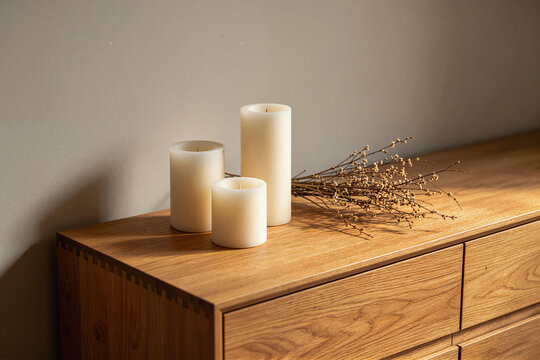 Three cream pillar candles and a bundle of dried twigs on a wooden sideboard