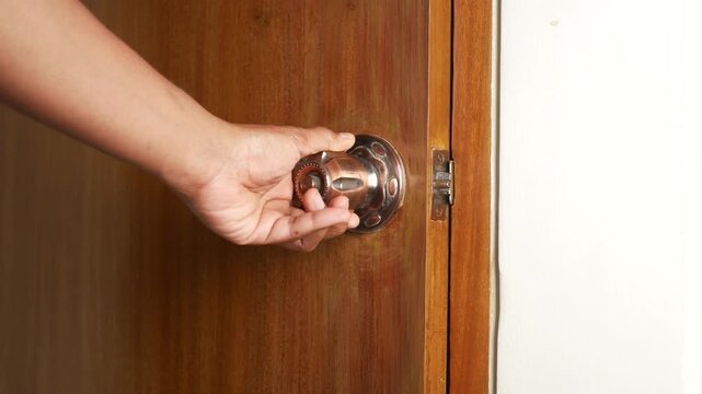 Close up of hand opening and closing wooden door with bronze knob in bright room