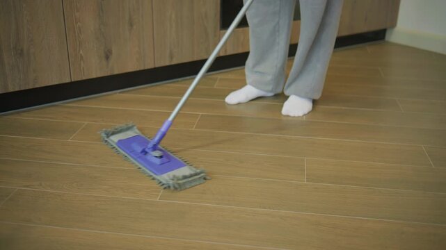 Cleaning the floor in a home setting with a mop during the afternoon hours while wearing comfortable clothing and socks