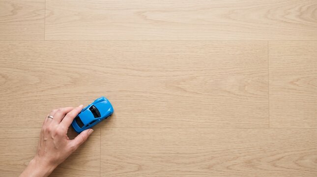 木目調のフローリングの上で青いミニカーを走らせて遊ぶ親子の手元   
