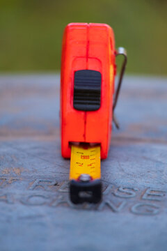 Close-up of an orange tape measure with a yellow blade resting on a rustic metallic surface outdoors