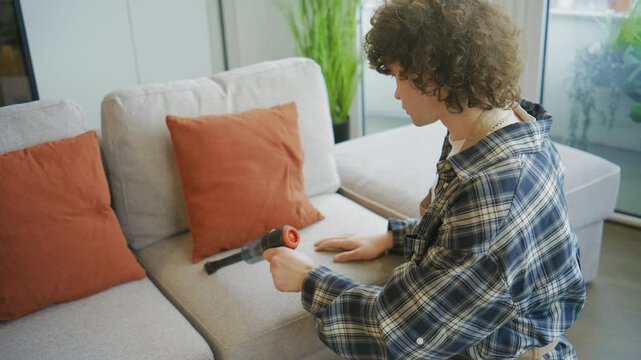 Person cleans sofa with handheld vacuum in living room during afternoon at home