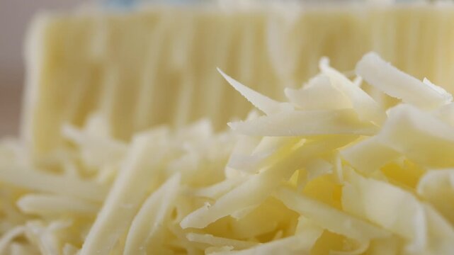 Freshly grated parmesan cheese on a kitchen counter with an out-of-focus cheese block in the background