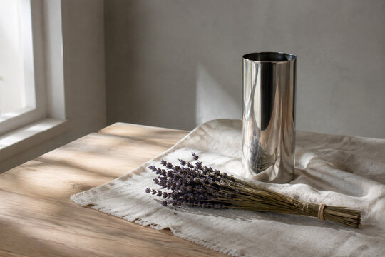 Silver cylinder vase and dried lavender on cream linen cloth on light oak table, minimalist home decor concept