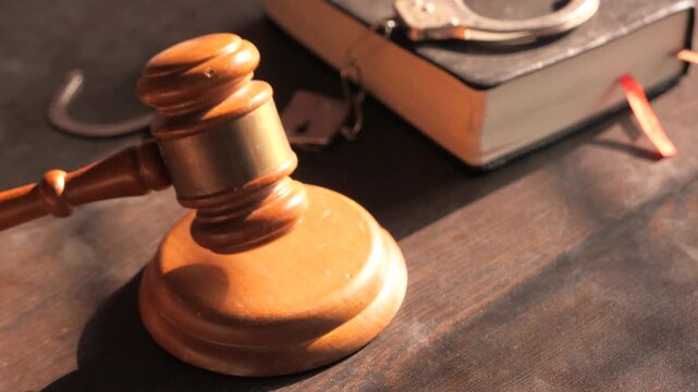 Wooden gavel hitting sound block on judge desk with handcuffs and law book background for justice concept