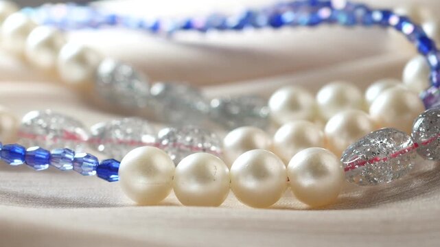 Close up shot of shimmering pearl necklaces and blue beads on elegant silk fabric, motion to the left