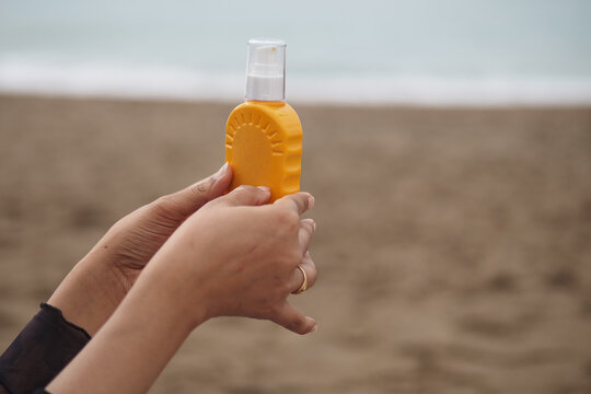 Person holds a yellow sunscreen bottle on a sandy beach in daylight