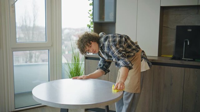 Young man cleans table in modern kitchen during daylight while maintaining focus on task in urban setting