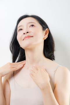 A woman in her 50s caring for her neck and d&eacute;colletage with both hands: A beauty image of middle-aged women practicing anti-aging and skincare