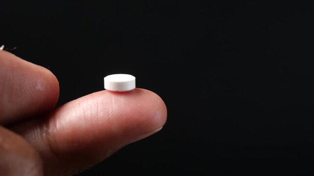 White tablet pill sitting on tip of human finger with dark background