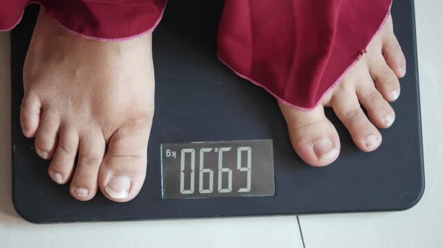 Woman stepping on digital scale to measure weight, footage shows progress