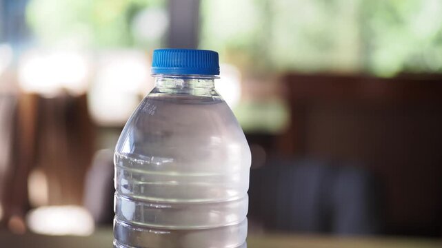 Close-up shot of a clear plastic bottle filled with refreshing water, with a vibrant blue cap, sitting on a wooden table in a well-lit indoor setting, showcasing a healthy and hydrating lifestyle
