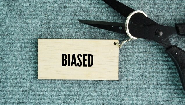 Scissors and wooden tags with the word biased. showing an unfair preference for or against someone or something, which prevents a neutral or objective point of view