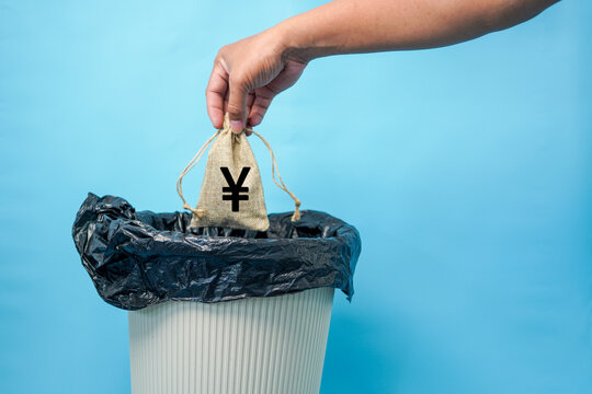 Hand dropping a small burlap sack with a Chinese yuan symbol into a black plastic trash bin