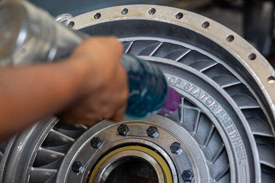 Mechanic hand sprays cleaning fluid on torque converter turbine wheel in industrial workshop.
