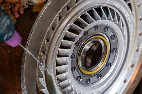 Mechanic hand sprays cleaning fluid on torque converter turbine wheel in industrial workshop.