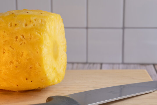 Fresh pineapple slice rests on wooden cutting board. Sharp knife lies beside it, ready for use. Ideal for tropical food, recipe