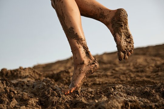Bare feet with mud caked on skin, walking through a muddy, textured terrain