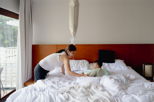 Asian mother and toddler son celebrating first birthday on white bed with cake and balloon