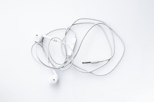Top-down view of messy tangled white wired earphones isolated on a white background representing frustration and disorganized technology.