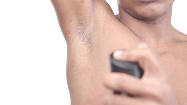 Young man applying deodorant spray to underarm for body hygiene and odor protection in slow motion