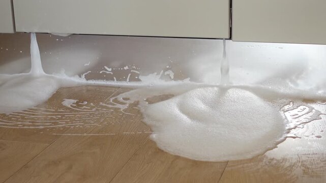 Dishwasher leaking soap bubbles on kitchen floor from appliance malfunction