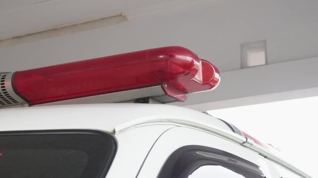 Close up view of a red emergency siren lightbar and speaker mounted on the white roof of an ambulance or police vehicle, emergency response equipment, public safety concept, and warning signal device.