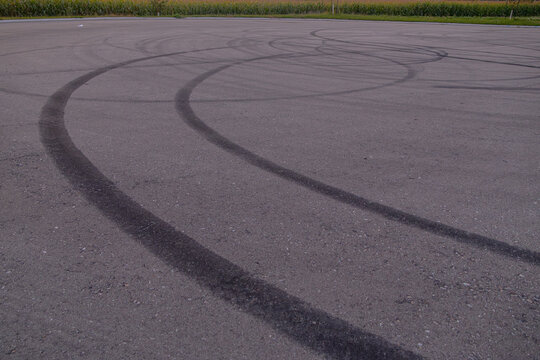 Tire skid marks on empty asphalt road with cornfield in background