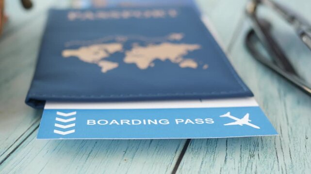 Camera panning across travel essentials including passport boarding pass and sunglasses on blue wooden table