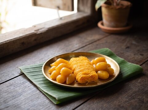 Thai golden egg yolk desserts thong yod, foi thong and med khanun on brass plate by window