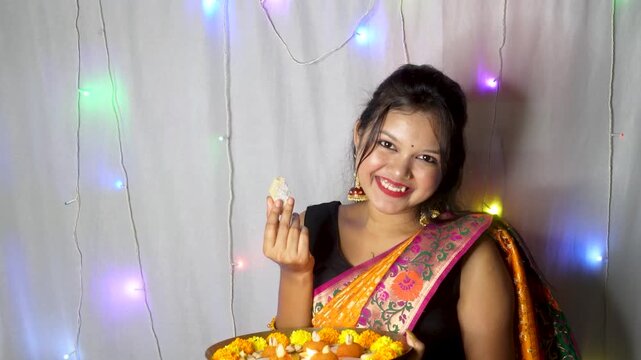 Indian young pretty woman eating Indian sweet - kaju katli barfi on the occasion of Diwali festival celebration. enjoying eating homemade sweets in the festival season.