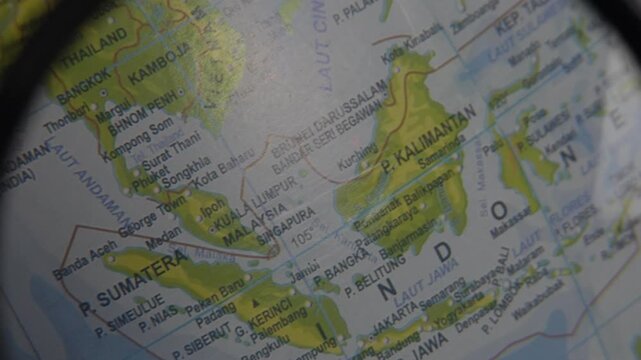 Close-up view of Southeast Asia map focusing on Indonesia, Malaysia, and Thailand through a magnifying glass, geography education, travel planning, navigation, and location search concept.   