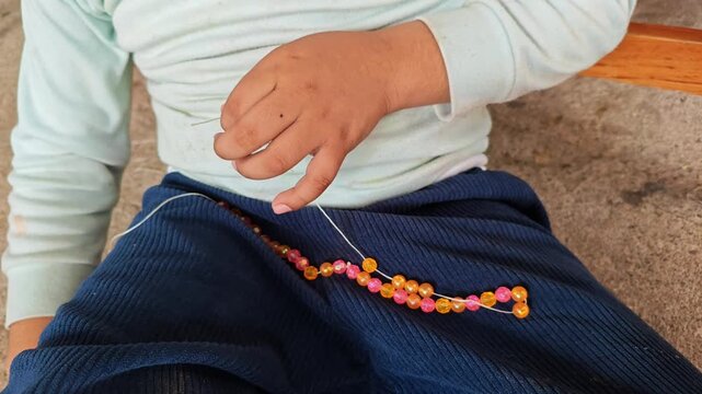 Hands Stringing Colorful Plastic Beads onto Thread to Make Handmade Necklace