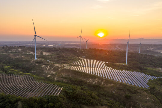 Wind turbines and solar panels on rolling hills at sunset