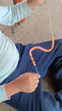 Child Threading Final Plastic Bead to Complete Handmade Craft Necklace