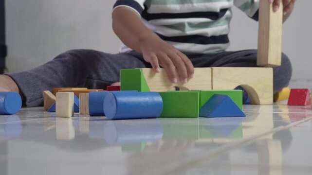 Close up view of a young child playing and building colorful wooden block toys on the floor, early childhood education concept, fine motor skill development, creative play, and home learning activity.