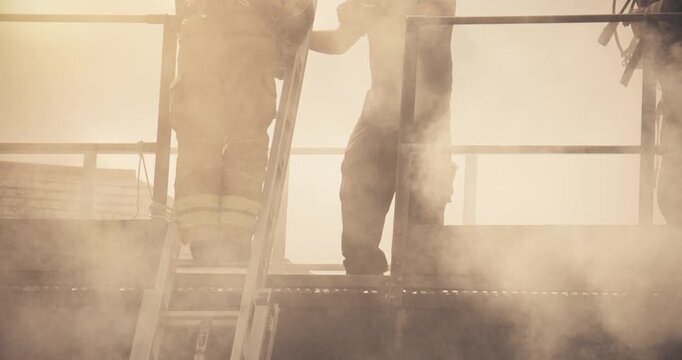 Firefighter crew &ndash; emergency service fireman rescue of victim. In uniform and gas mask in response to fire with firefighting ladder against burning building releasing smoke with casualty.