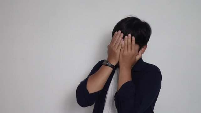 Shocked Asian man looking at his wristwatch with wide eyes and open mouth in panic, running late, missed deadline, and urgent time management concept against plain white background.