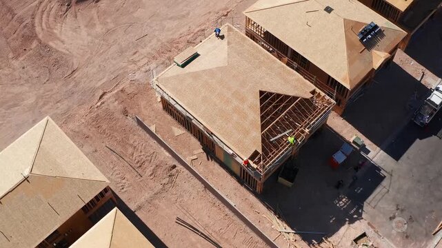 Aerial top down view of construction workers building wooden roof framing and decking for a new residential suburban housing project